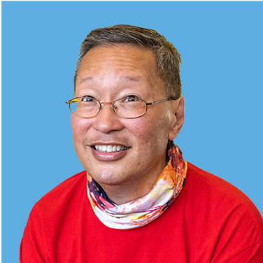 Smiling person, wearing glasses, a red shirt, and a scarf, against a light blue background.