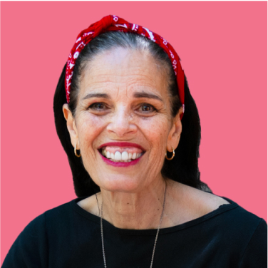 Smiling person wearing a red bow in their hair and a black shirt, against a pink background.