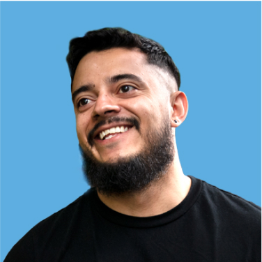 Smiling person with short hair and a beard, wearing a black shirt, against a light blue background.